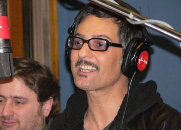 Foto di Roberto Priolo. [Fiorello a Viva Radio2 (sullo sfondo Riccardo Cassini, uno degli autori del programma radiofonico) nel 2006 (https://upload.wikimedia.org/wikipedia/commons/4/45/Fiorello.jpg)]. Attraverso Wikipedia